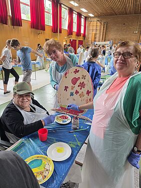 3 Frauen zeigen, wie weit sie ein hölzernes Osterei schon angemalt haben