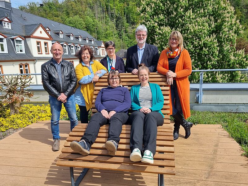 Gruppenfoto auf dem zwei Personen auf einer Bank sitzen und die anderen dahinter stehen. 