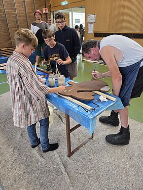 mehrere Jungen und ein Mann pinseln einen Osterhasen aus Holz an