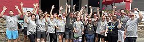 Viele fröhliche Menschen recken ihre Arme in die Höhe und jubeln. Die tragen Sporttrikots.
