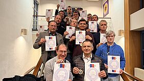 Eine Gruppe Menschen hält Urkunden in die Kamera.