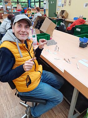 Ein lächelnder Mann zeigt Aufstellfiguren, die er aus Pappe ausschneidet.