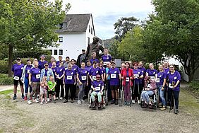 Eine große Gruppe von Menschen steht vor einem Denkmal. Die meisten tragen lilafarbene Laufshirts.