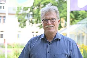 Ein Mann mit Brille im mittleren Alter. Kopf und Schultern sind zu sehen. Er ist draußen.