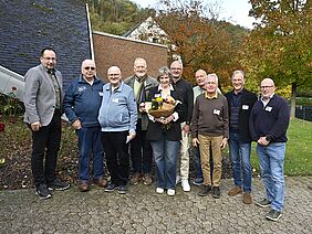 Eine Gruppe von Menschen steht zusammen. Die Dame in der Mitte hält einen Blumenstrauß in den Händen.
