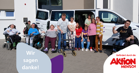 Ein Dutzend Menschen mit Beeinträchtigung steht oder sitzt im Rollstuhl vor einem weißen Bus.