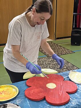eine junge Frau bemalt eine Holzblume in rot und gelb