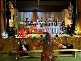 Auf einer Bühne tanzt eine Garde zu Karneval, vor der Bühne tanzt eine Zuschauerin mit