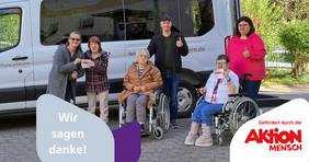 Sechs Menschen stehen vor einem weißen Fahrzeug. Zwei davon sitzen im Rollstuhl. Einige recken den Daumen nach oben, andere halten Aufkleber der Aktion Mensch in der Hand.