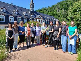 Elf Frauen stehen auf einer Dachterrasse im Freien. Im Hintergrund ist ein Haus zu sehen.