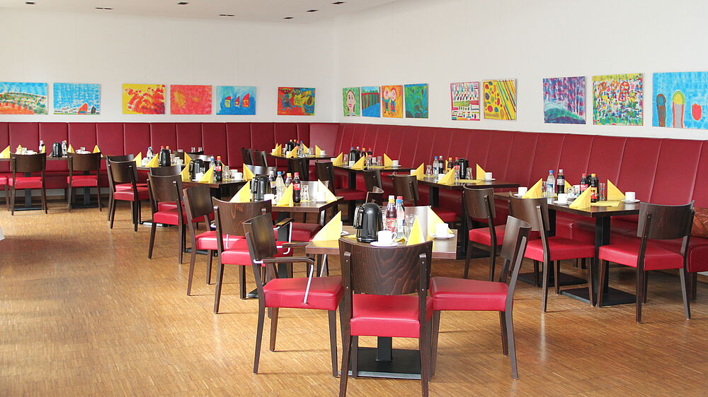 Das Bistro Orgelpfeife wartet mit gedeckten Tischen, dunkelroten Sitzgelegenheiten und bunten Bilder.