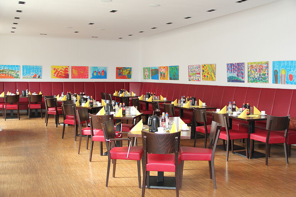 Das Bistro Orgelpfeife wartet mit gedeckten Tischen, dunkelroten Sitzgelegenheiten und bunten Bilder.
